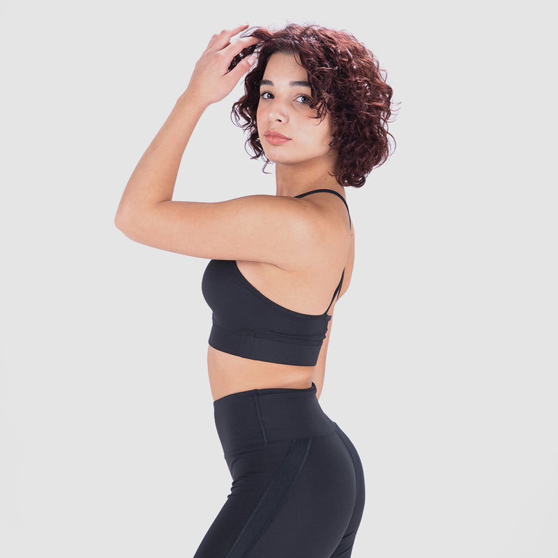 A person in a black sports bra and leggings poses sideways against a neutral grey background