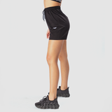 a fit woman stand at right and wearing short black with shoes ,plus the background is light grey 