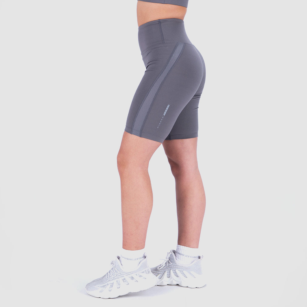 a fit woman stand at right and wearing seamless short grey with shoes white plus the background is light grey 