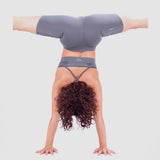 Person performing a handstand with legs spread wide apart, wearing a matching grey sports outfit consisting of a sports bra and fitted shorts