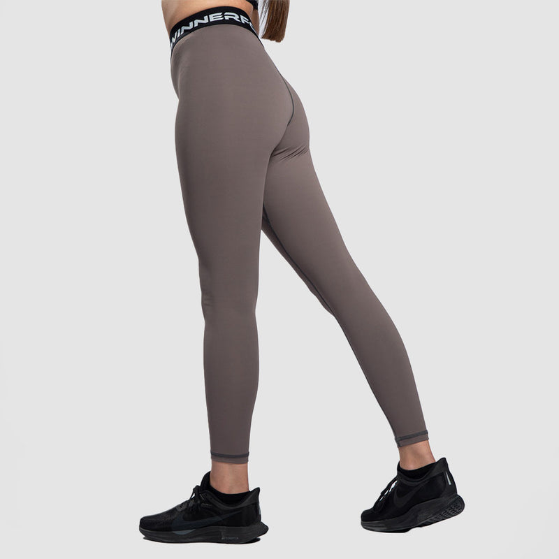 a fit woman stand at right  and wearing  legging  brown  with sneakers black 
