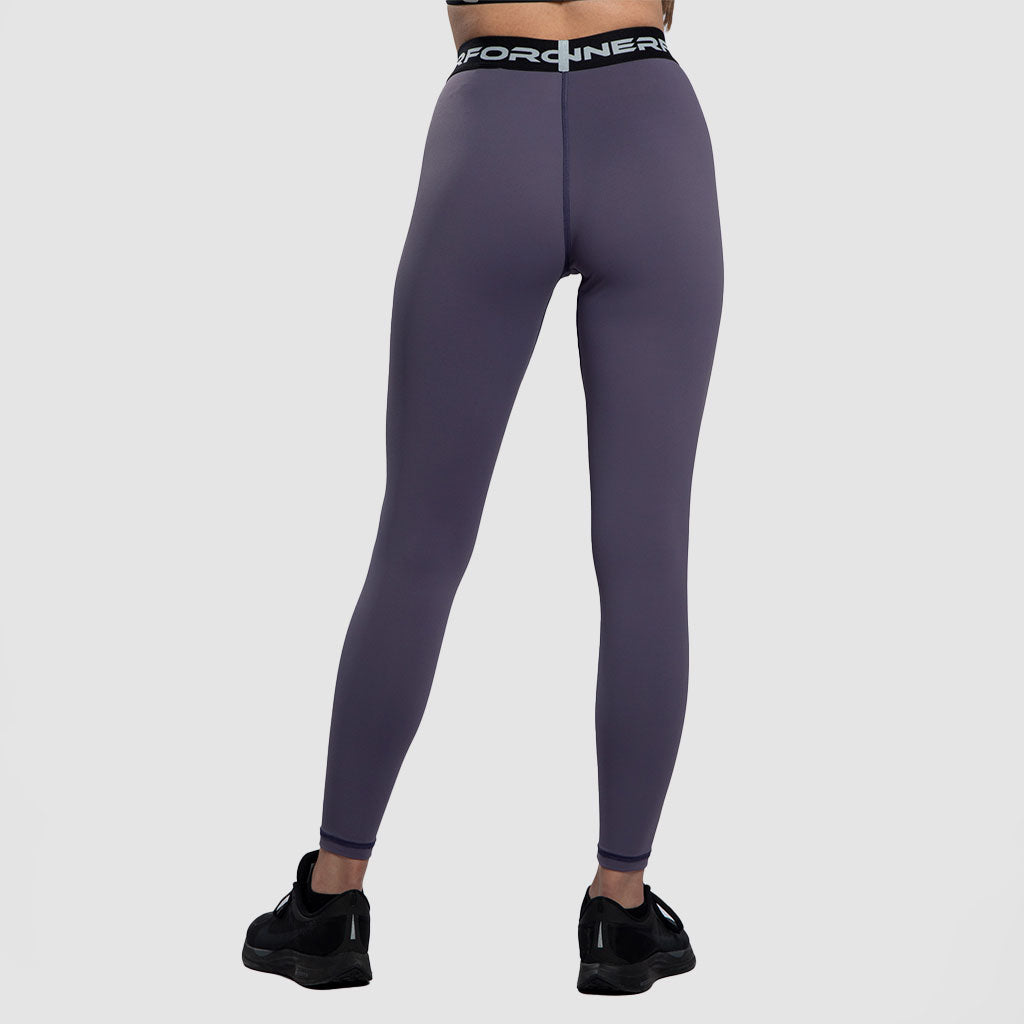 A back view for  woman with a fit physique ,she wearing a purple  legging  with black elastic bands featuring white text, She is also wearing black athletic shoes ,plus the background is light grey 