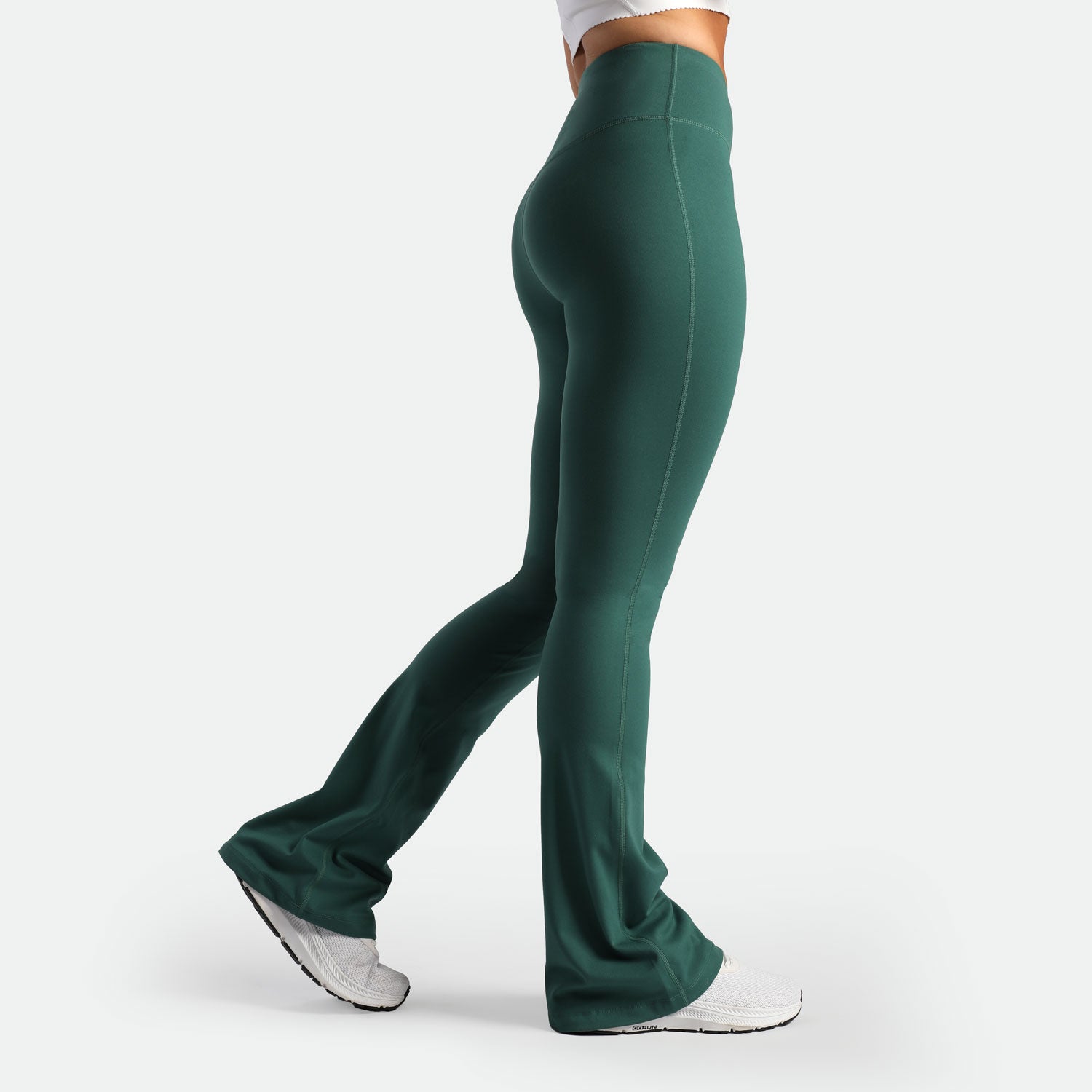 a fit woman stand at right and wearing flared legging posy green with shoes white 