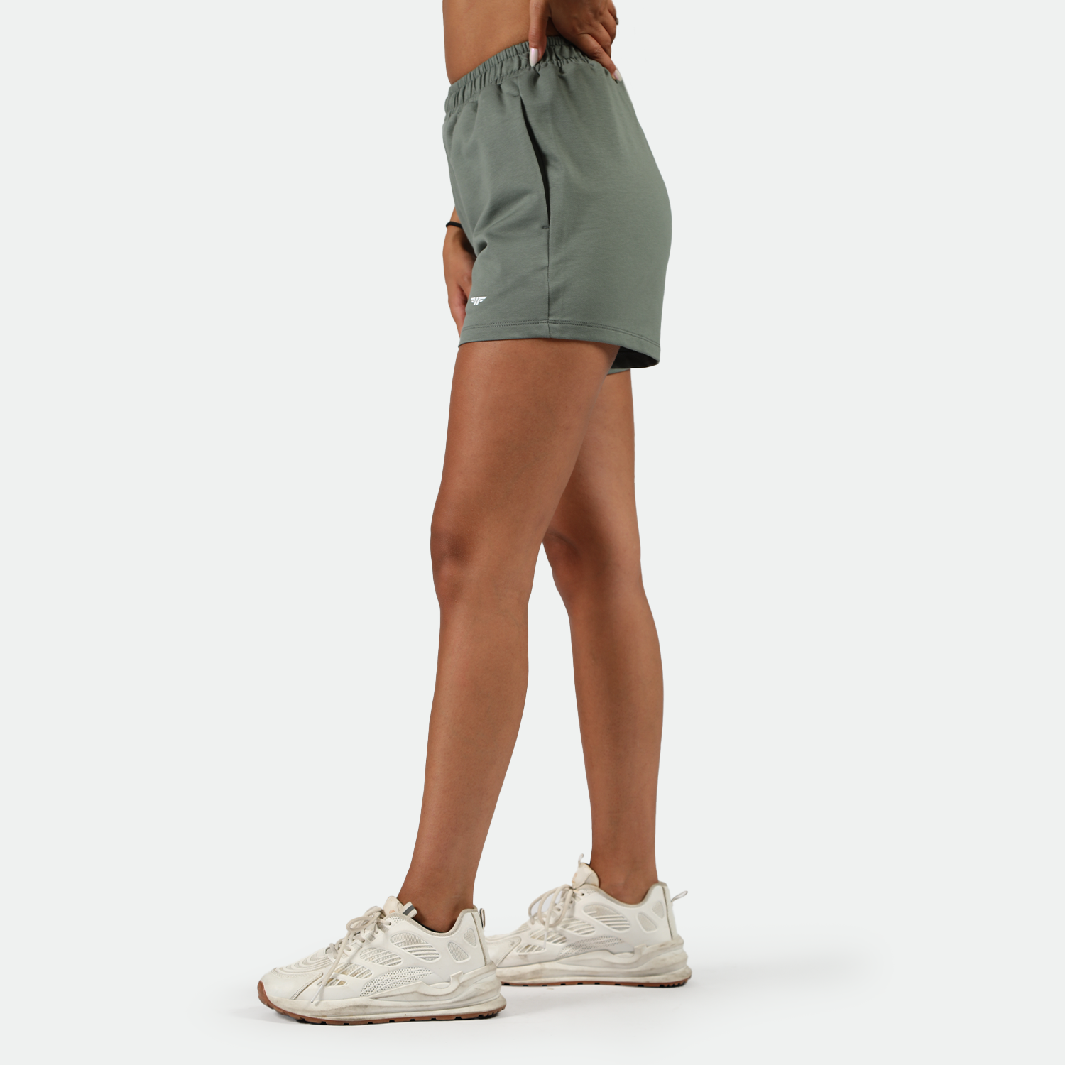 a fit woman stand right and wearing 
agave green  short with shoes ,plus the background is light grey 
