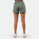 a back view for fit woman wearing 
 agave green short with shoes white ,plus the background is light grey 