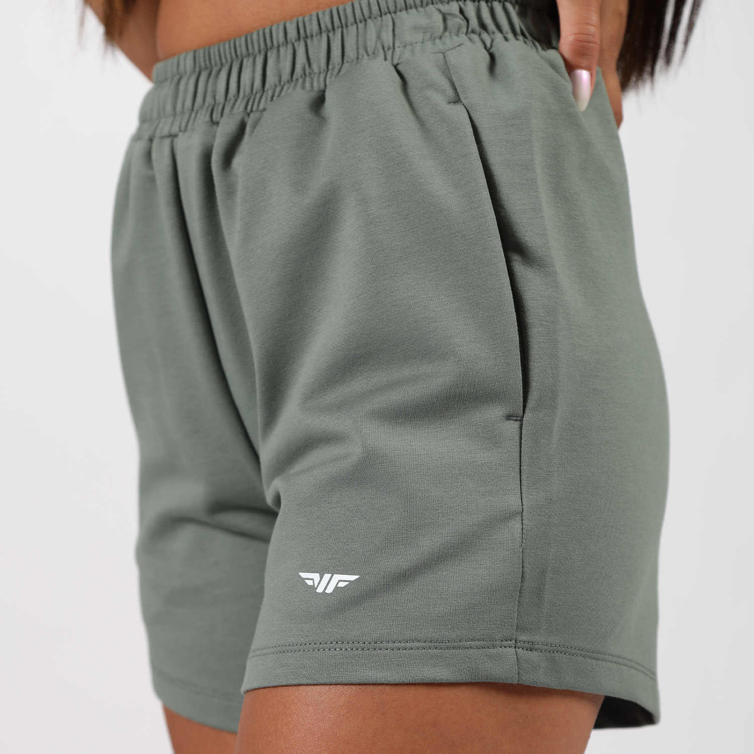 close up view for fit woman  wearing short green with logo ,plus the background is light grey 