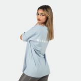 a fit woman stand at right and wearing t-shirt blue with logo and legging grey 