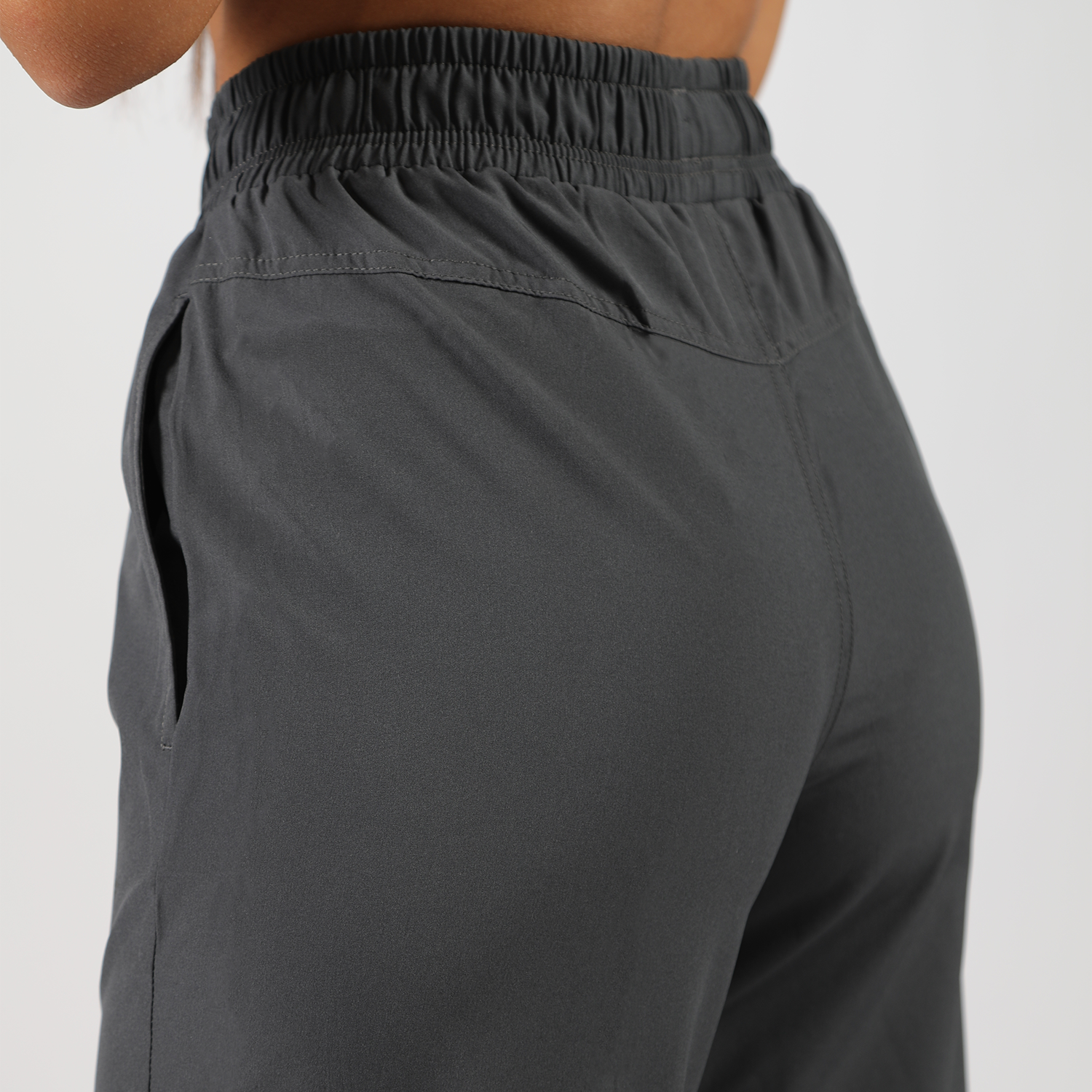 a back view for  fit woman wearing pants grey ,plus the background is light grey 