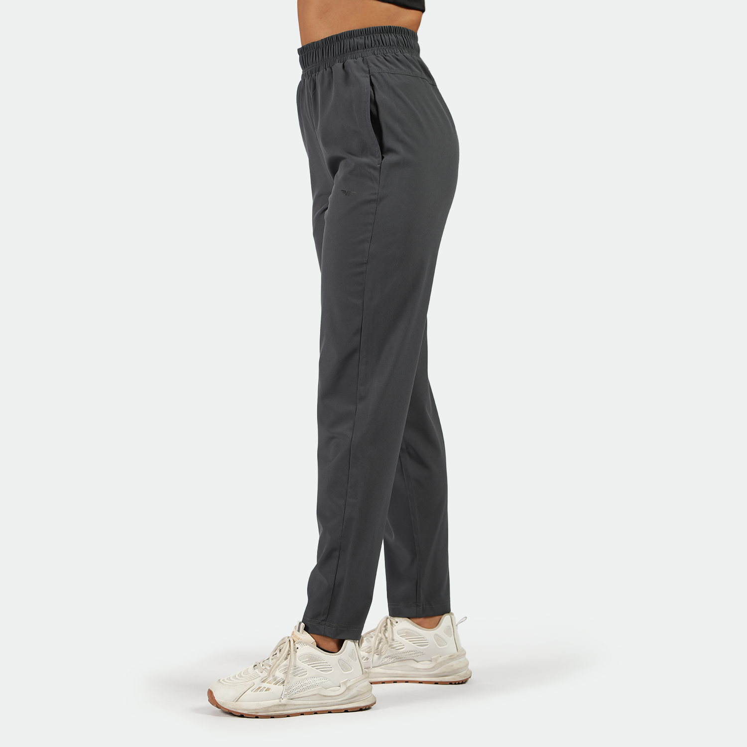 a fit woman stand at right and wearing pants grey white athletic shoes, plus the background is light grey 
