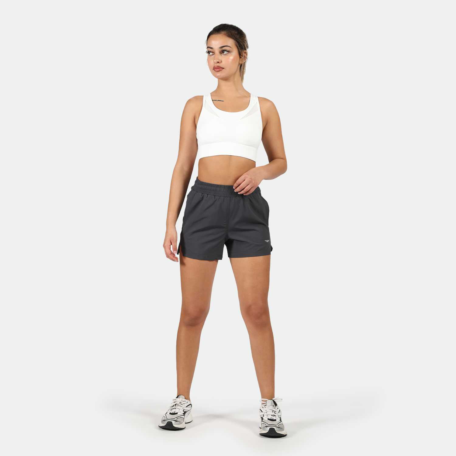 a fit woman wearing sports bra white  with short grey ,and she wearing shoes ,plus the background is light grey 