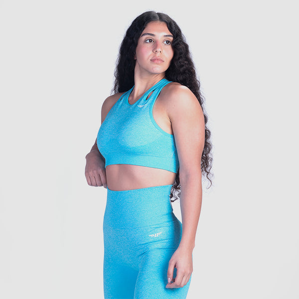 A woman with long, curly hair poses confidently, wearing a fitted, bright blue athletic outfit against a plain gray background.