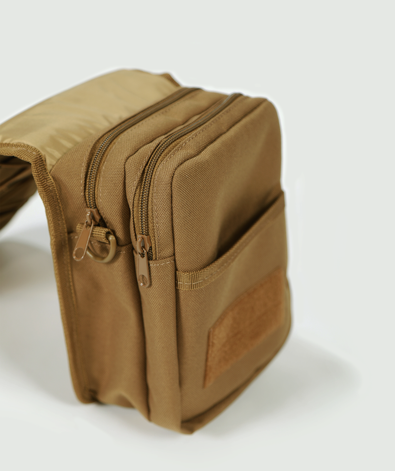 A tan-colored, rectangular, fabric waist pouch with multiple zippered compartments and a front pocket, resting on a white surface.