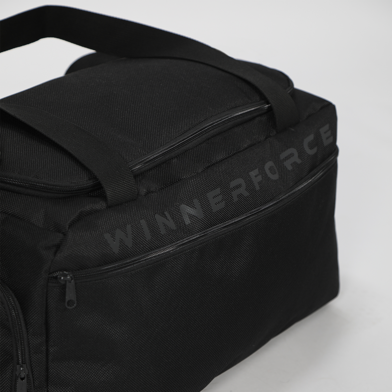 Black duffel bag against a light background. It features zippers, short handles, and a shoulder strap, conveying a sleek and functional design.