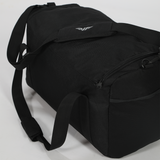 Black duffel bag with reinforced shoulder strap and zipper pocket on white background. Minimalist design with subtle logo, conveying functionality.