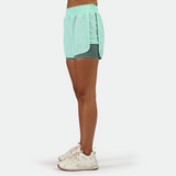a fit woman stand at right and wearing  beach glass blue short 2 in 1 with shoes  white ,plus the background is light grey 