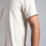Close-up of a person wearing a short-sleeve crew-neck t-shirt in off-white or cream, showing the side seam .