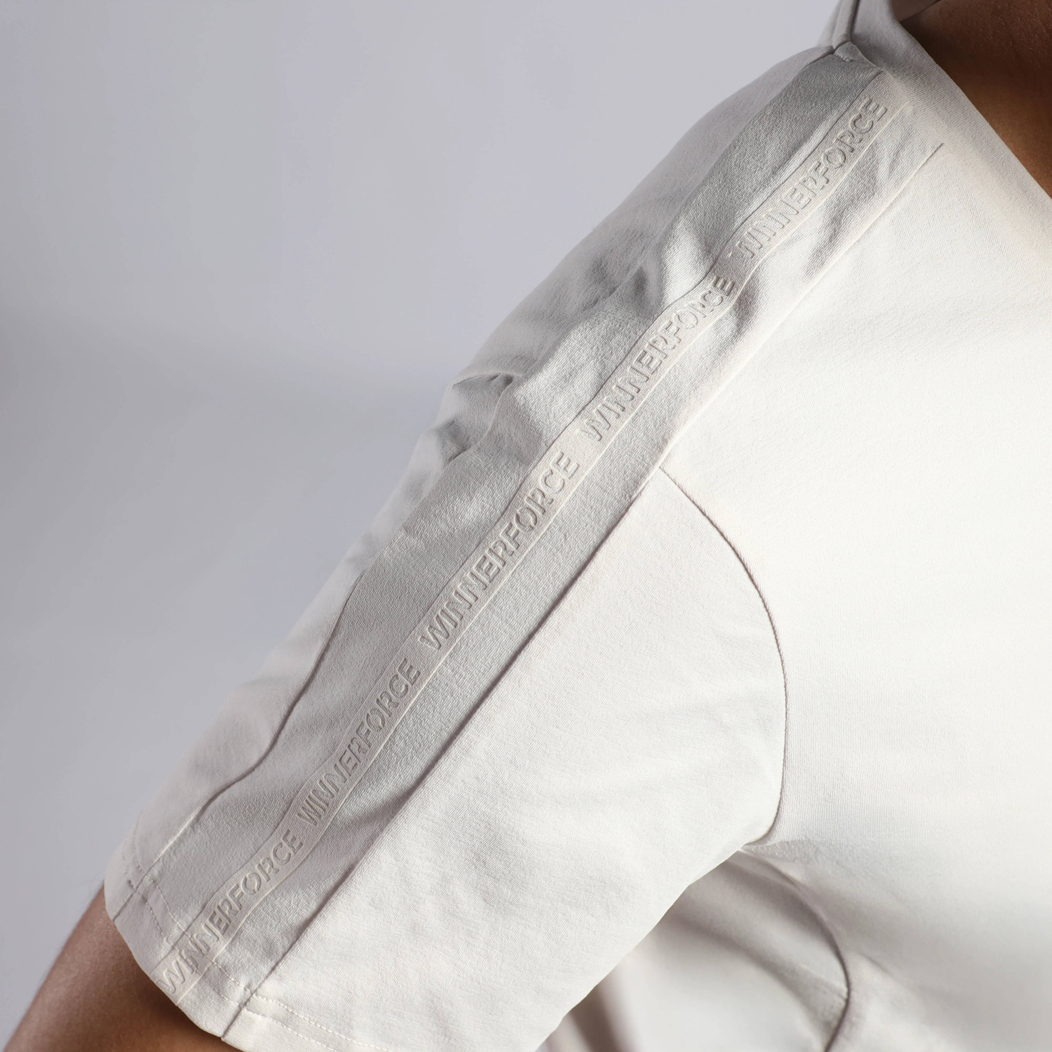 Close-up of a person wearing a white short-sleeve top, showing the sleeve with a repeating embossed 'winnerforce' brand name along the seam.