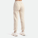 a back view for woman wearing jogger pants beige with  white shoes athletic ,plus the background is light grey 