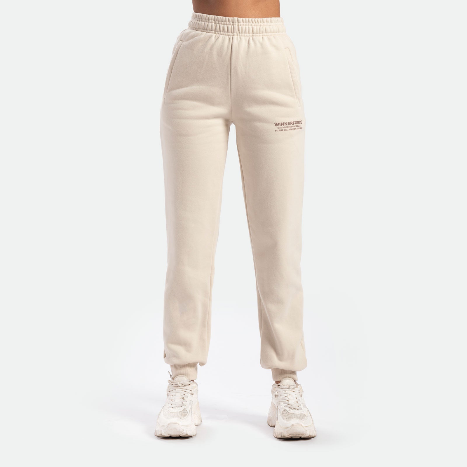 a fit woman wearing jogger pant beige with logo ,she wearing white shoes  athletic, plus the background is light grey 