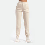 a fit woman wearing jogger pant beige with logo ,she wearing white shoes  athletic, plus the background is light grey 