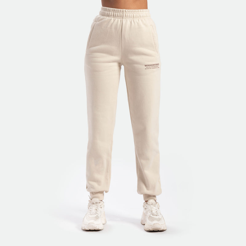 a fit woman wearing jogger pant beige with logo ,she wearing white shoes  athletic, plus the background is light grey 