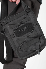 close up view  for  small, black crossbody shoulder bag with an adjustable strap, front elastic cord, and a subtle logo on the front, displayed against a plain light gray background.