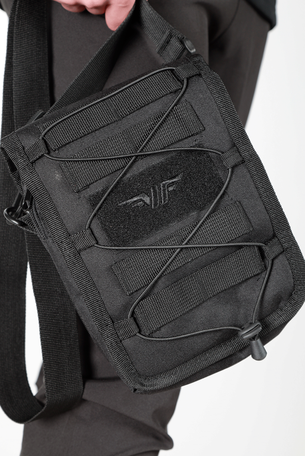 close up view  for  small, black crossbody shoulder bag with an adjustable strap, front elastic cord, and a subtle logo on the front, displayed against a plain light gray background.