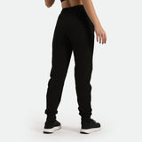 a back view for fit woman wearing black jogger pants with shoes , plus the background is light grey 