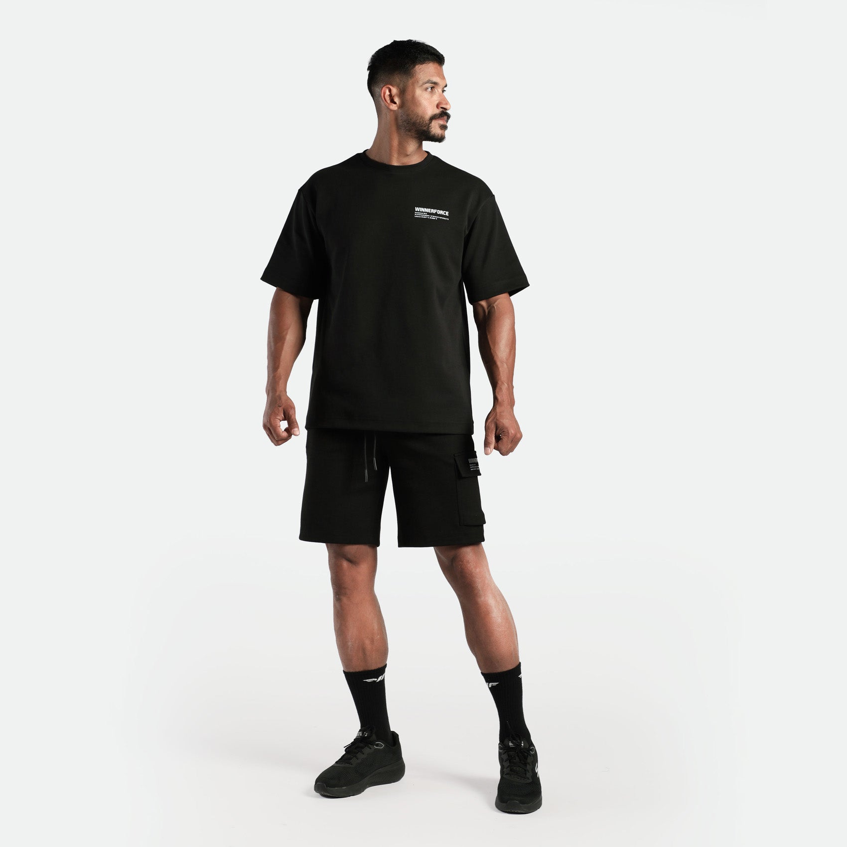 a fit man stand  with pose and look at right ,he wearing matching set black  t-shirt and short ,plus shoes with socks 
