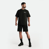a fit man stand  with pose and look at right ,he wearing matching set black  t-shirt and short ,plus shoes with socks 