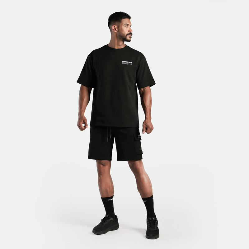 a fit man stand  with pose and look at right ,he wearing matching set black  t-shirt and short ,plus shoes with socks 