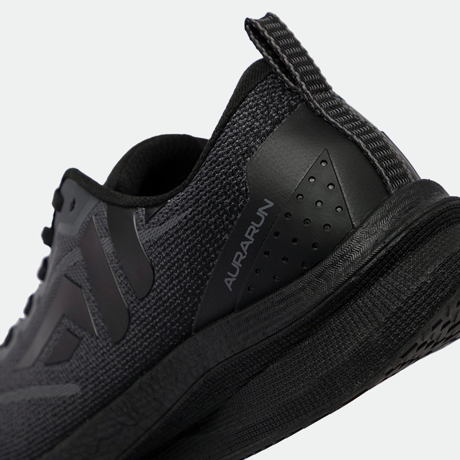 Close-up of a sleek, black athletic shoe from the heel angle, showcasing a textured, breathable mesh design and subtle branding text "AurA Run."