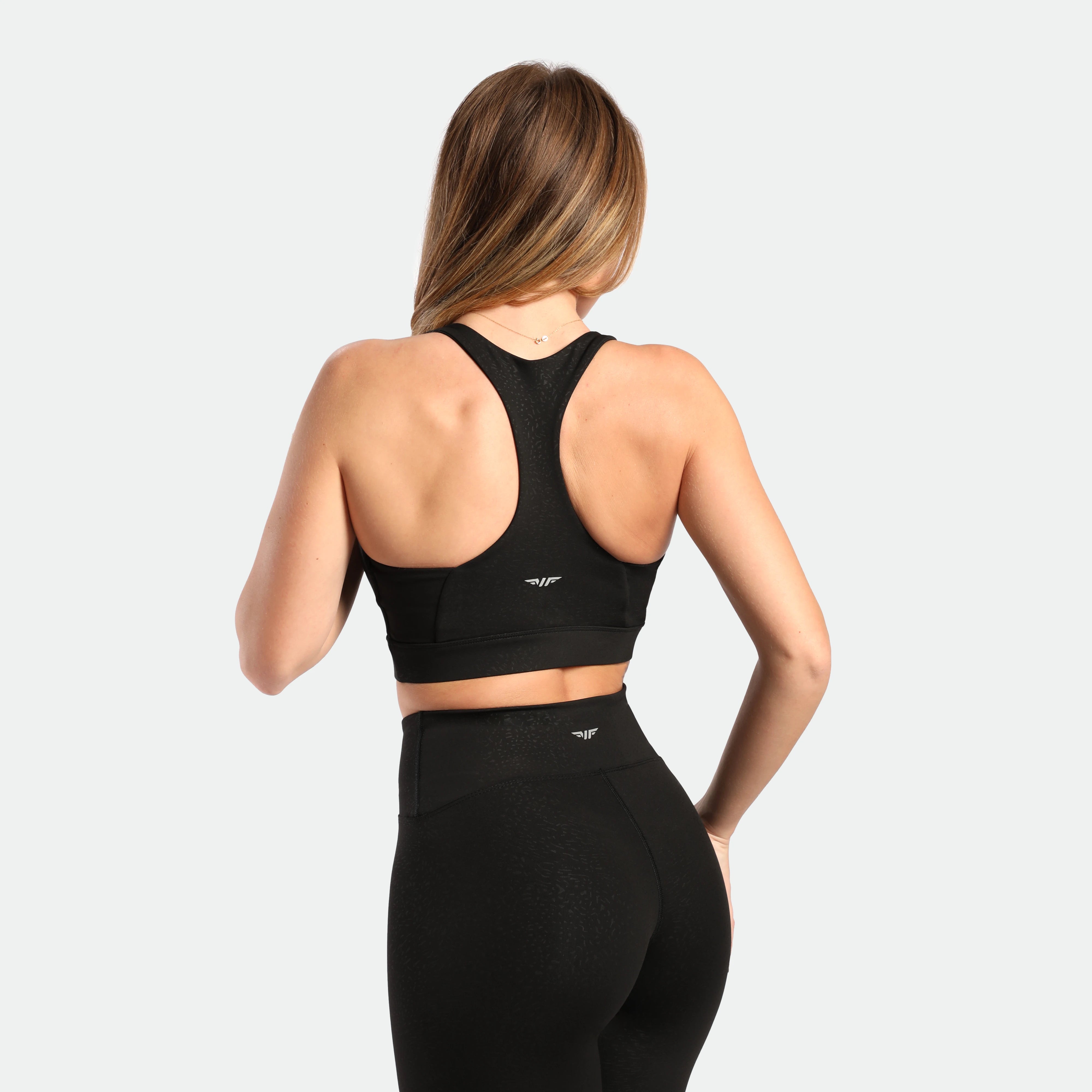 a back view for fit woman wearing matching set black ,bra and legging ,plus the logo