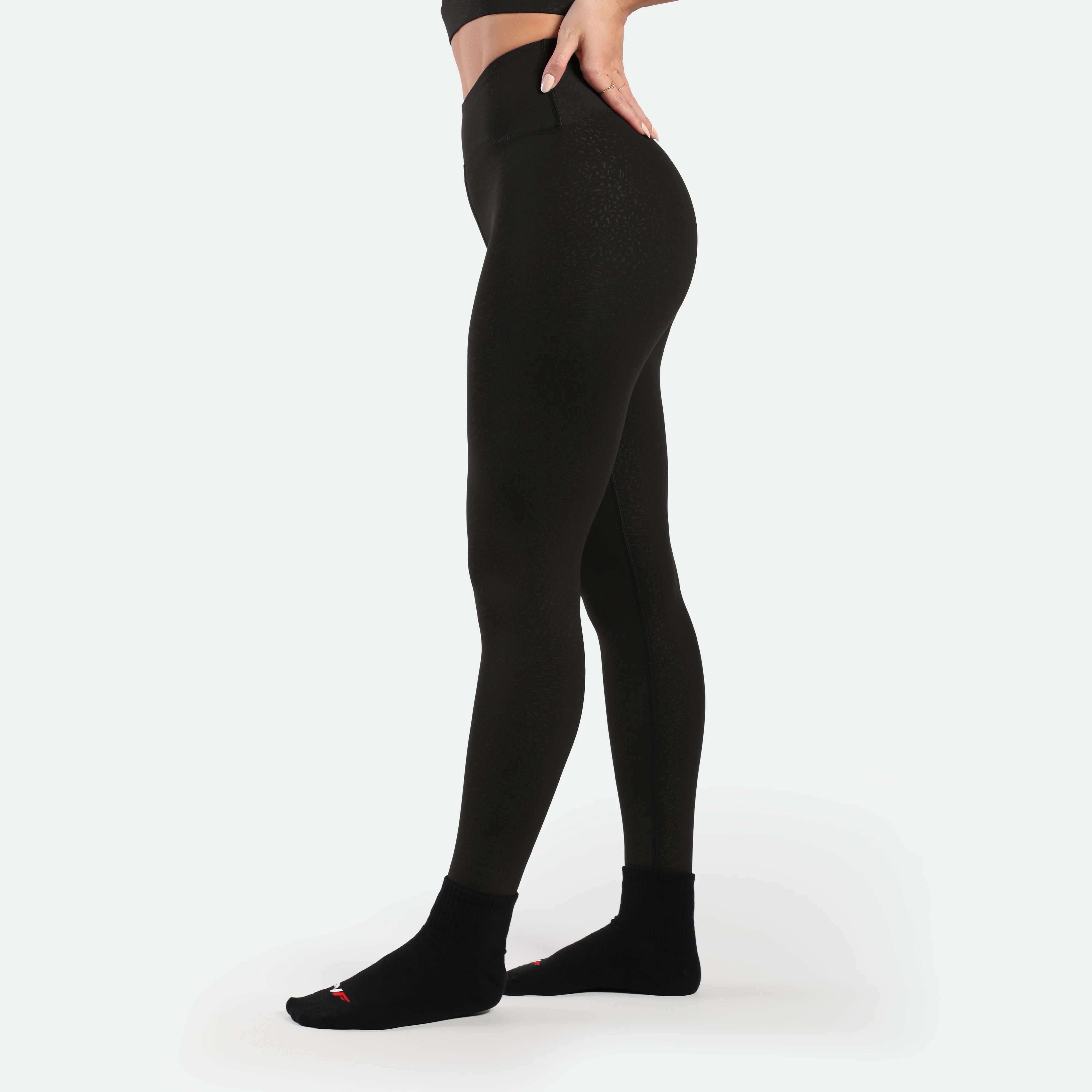 a fit woman stand at right and wearing legging black with  socks black 