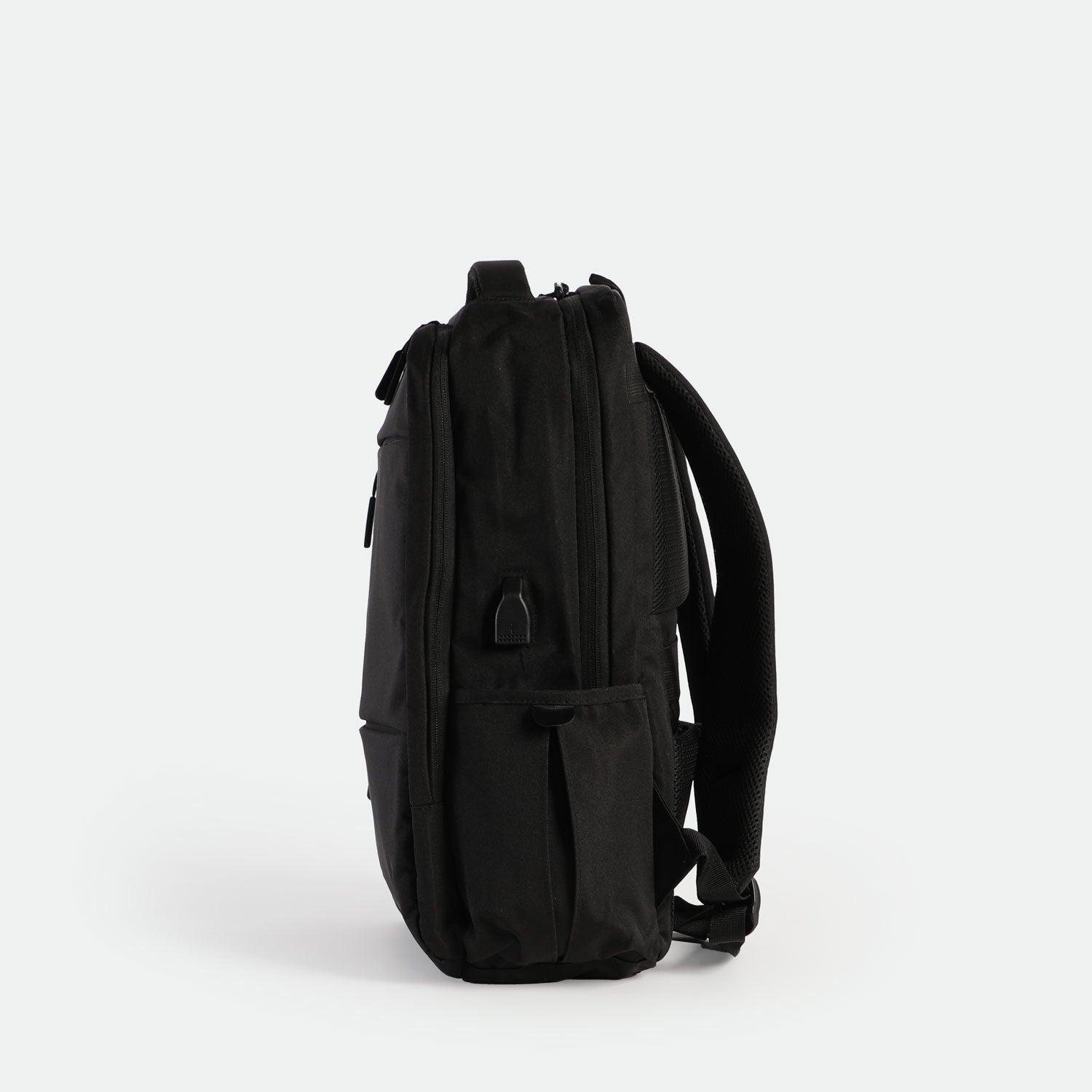 A sleek, black backpack is shown standing upright on its base, viewed from the side against a plain white background. The design is minimalist with subtle zippers and padded shoulder straps visible.