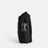A black backpack with a mesh side pocket containing a black and gray water bottle. The backpack is shown from a side view, highlighting its multiple compartments and sleek design
