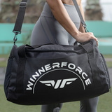 A person in gray leggings carries a black duffel bag with "WINNERFORCE" printed on it. The scene conveys an active, sporty vibe.