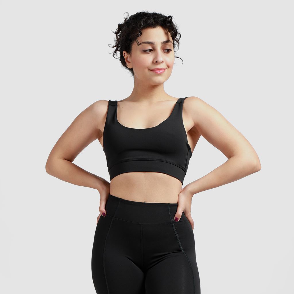 Woman wearing matching bra and leggings, standing and looking to the right, light gray background
