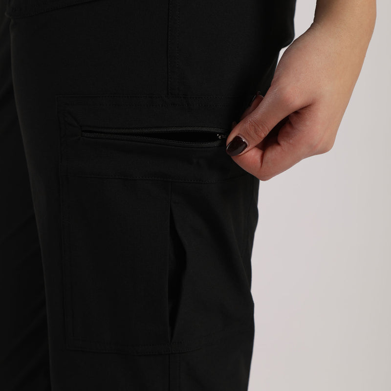 Close-up of a hand with dark nail polish opening a black zipper pocket on dark pants. The background is plain,