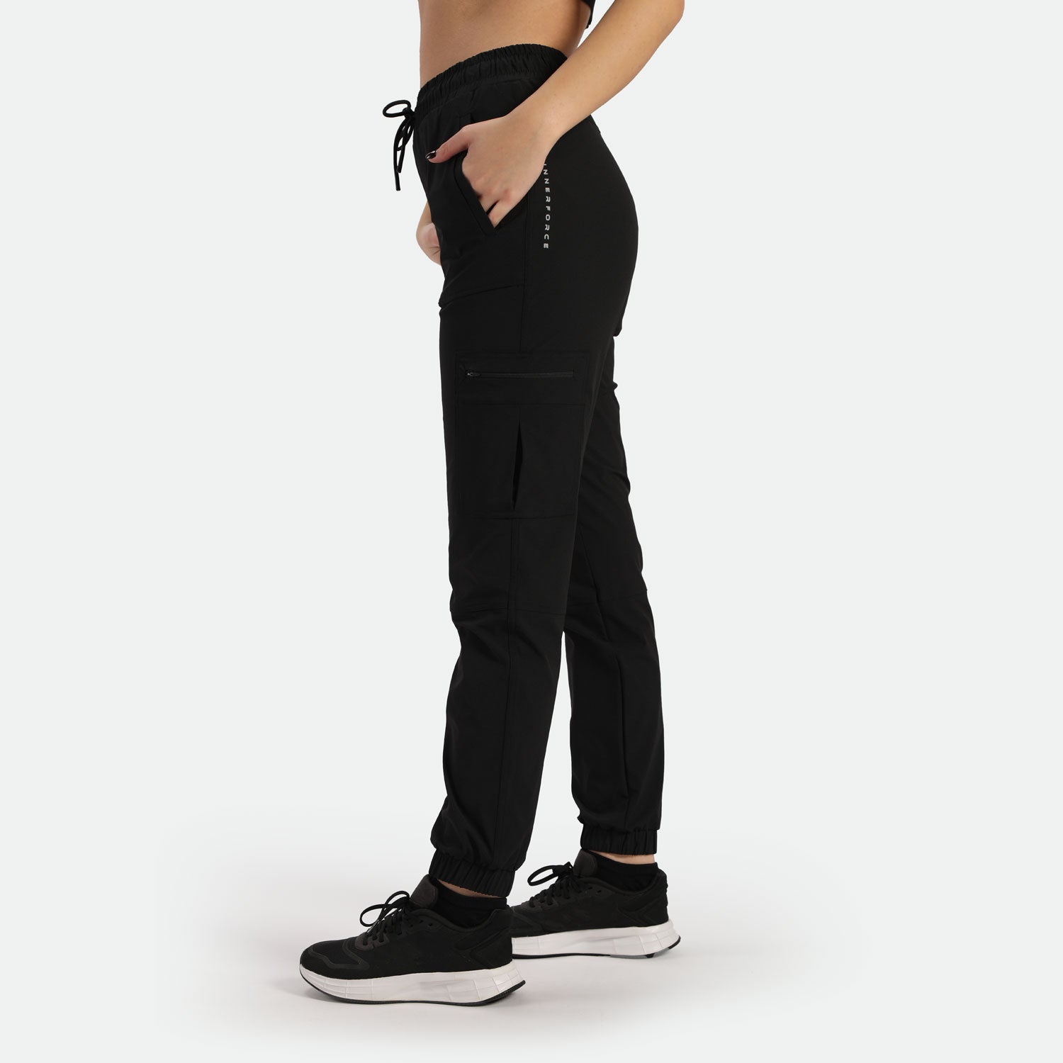 a fit woman stand at right and wearing 
 black cargo pants with shoes ,plus the background is light grey 
