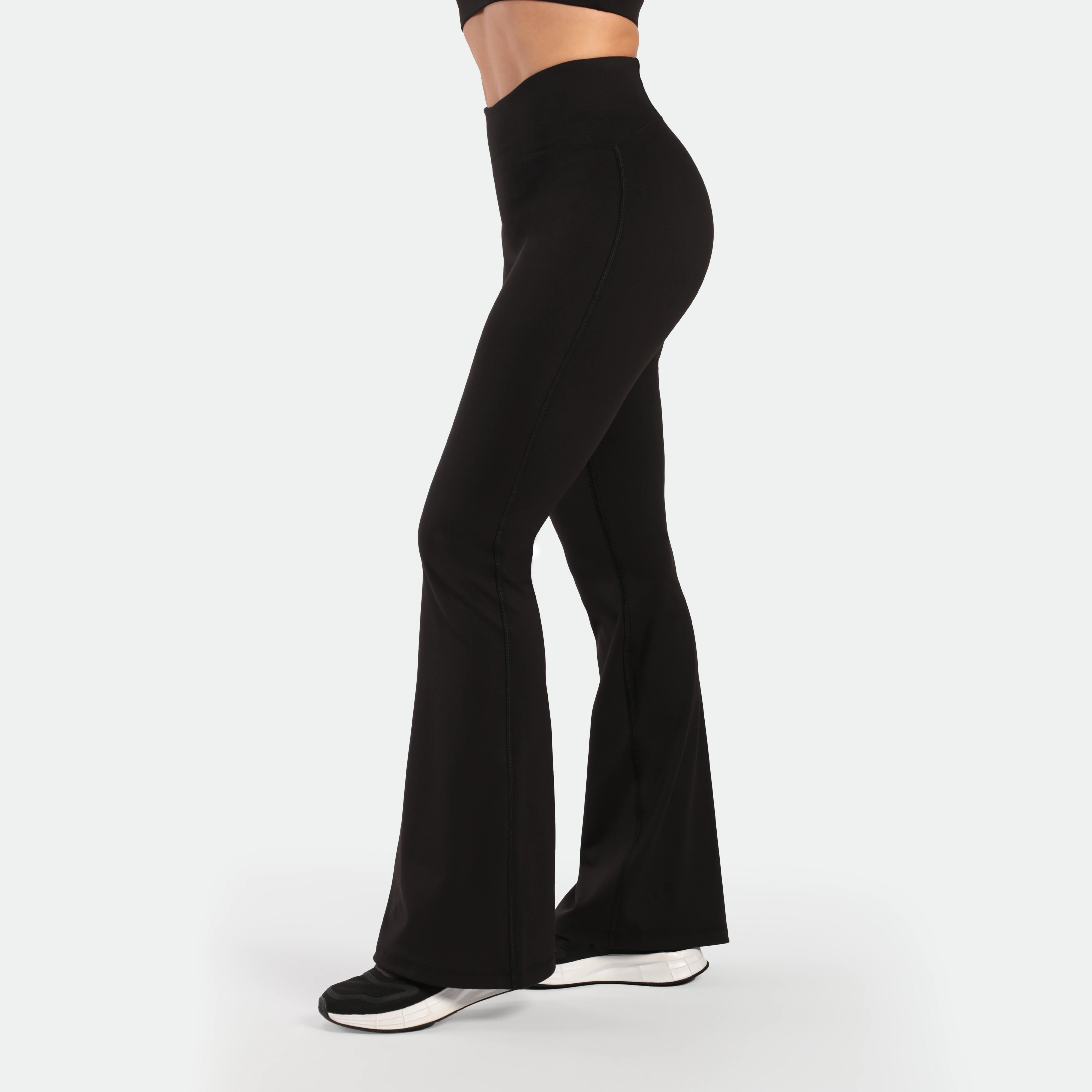 a fit woman stand at right and wearing matching set black ,bra and flared legging  , plus the shoes 