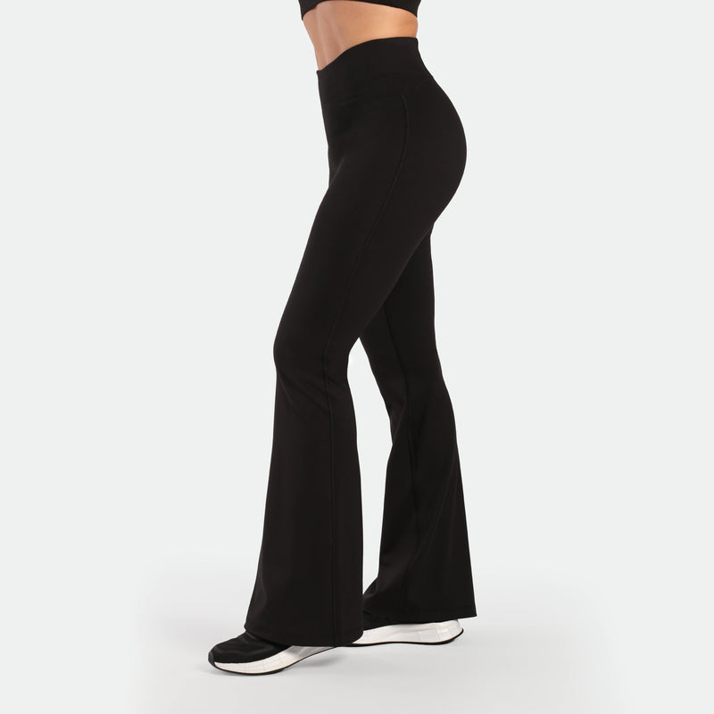 a fit woman stand at right and wearing matching set black ,bra and flared legging  , plus the shoes 