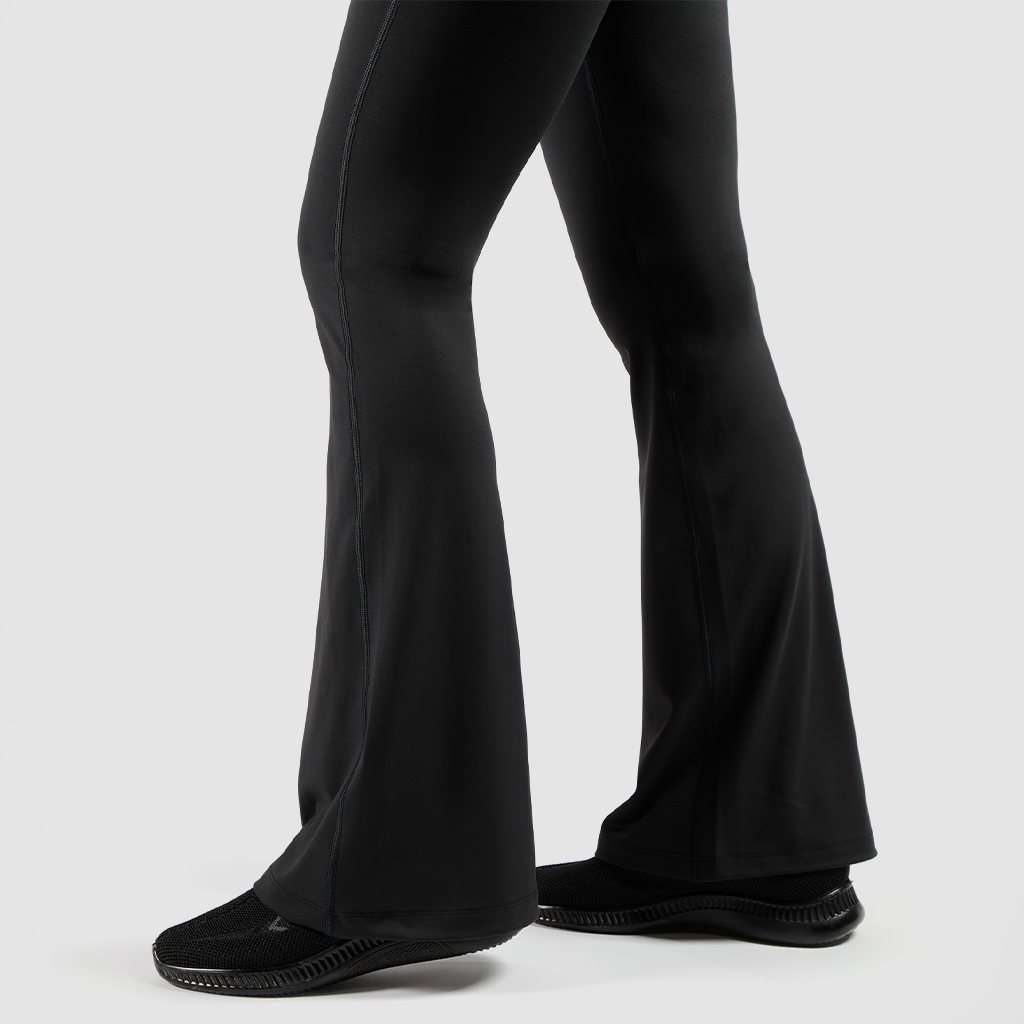 a fit woman stand at right and she wearing  flared legging  with shoes black ,the background is light grey 