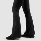 a fit woman stand at right and she wearing  flared legging  with shoes black ,the background is light grey 
