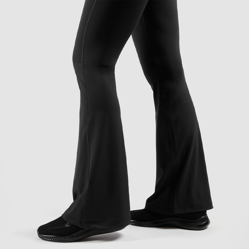a fit woman stand at right and she wearing  flared legging  with shoes black ,the background is light grey 