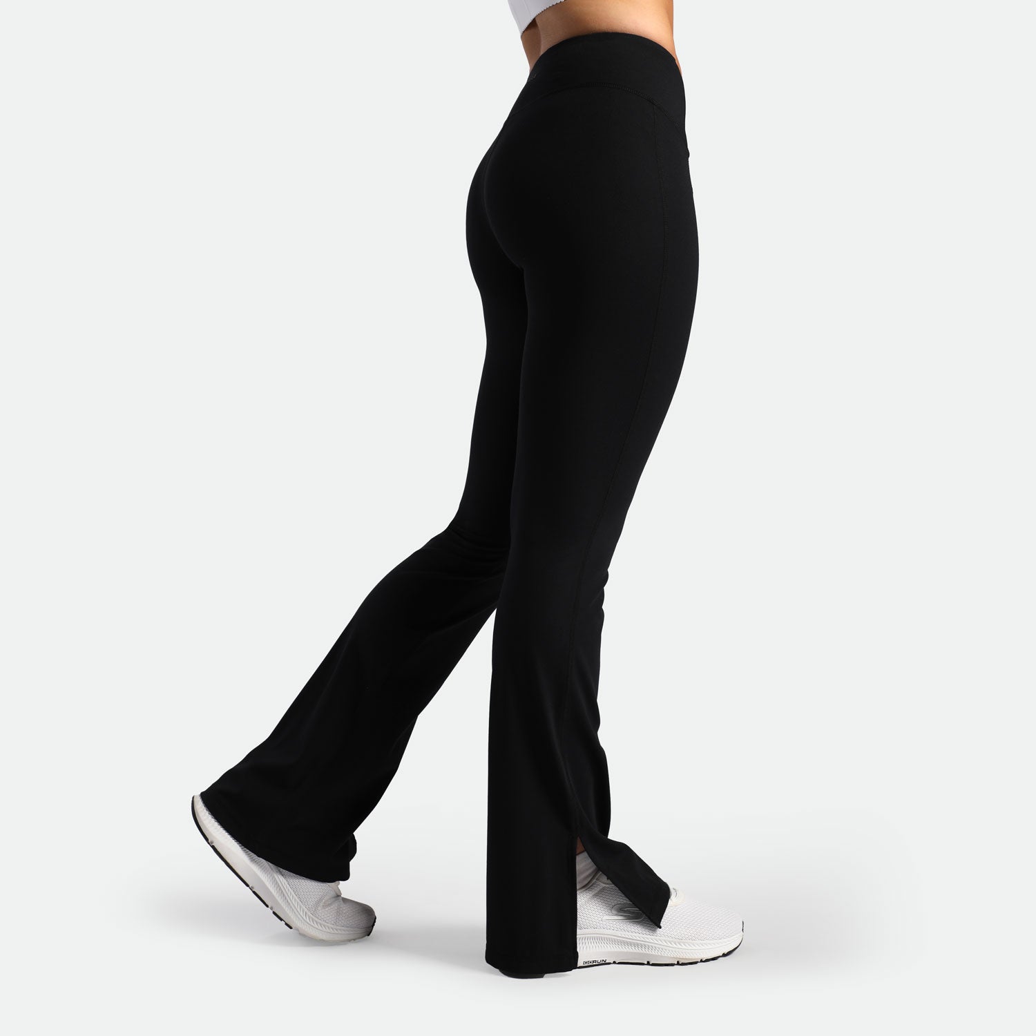 a fit woman stand at right and wearing flared legging black with shoes white 