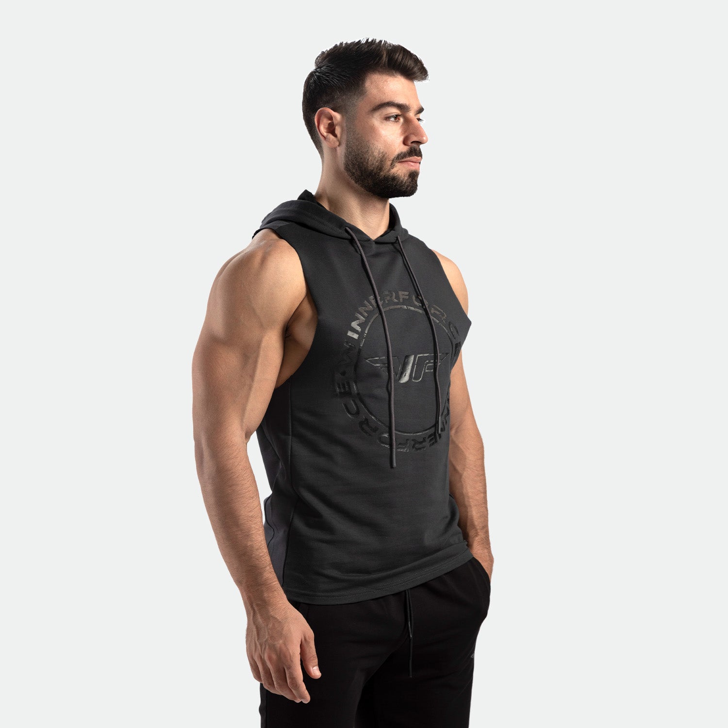 a fit man stand at right and wearing half hoodie  shadow black with logo, plus pants black 