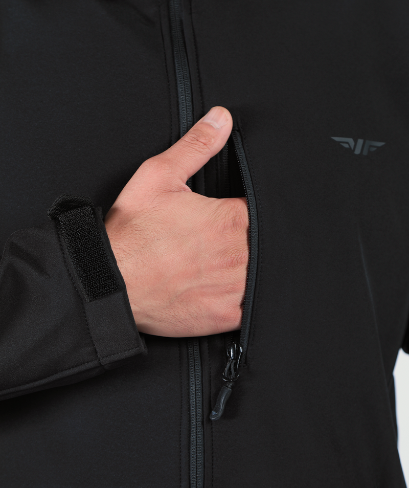 A close-up of a person's hand placing it inside the chest pocket of a black men's Apollo jacket with a secure zipper and adjustable Velcro wrist strap.