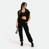 a fit woman stand at right and wearing matching set  black , bra pants and shoes ,plus bottles green 
