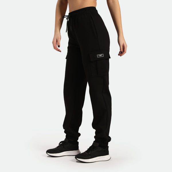 a fit woman stand at right ,she wearing jogger pant black ,shoes black ,plus the background is light grey 